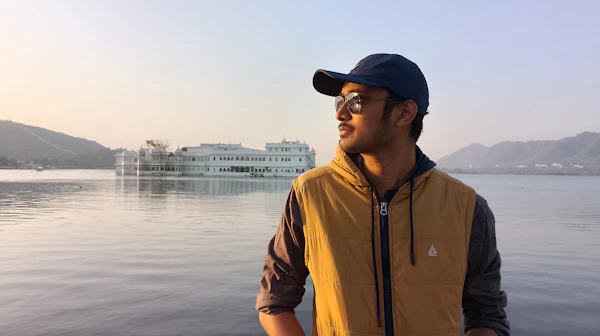 A man standing on a boat with the lake behind him in warm light