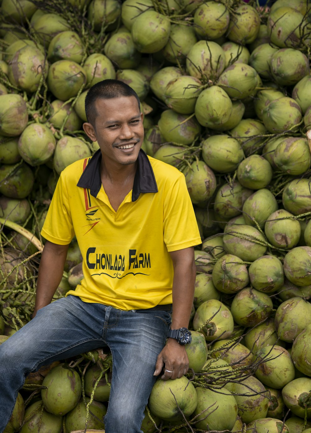 um homem sentado em cima de uma pilha de cocos