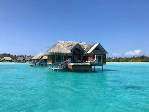 A tranquil overwater bungalow in the Maldives surrounded by crystal-clear blue sea under a bright sky.