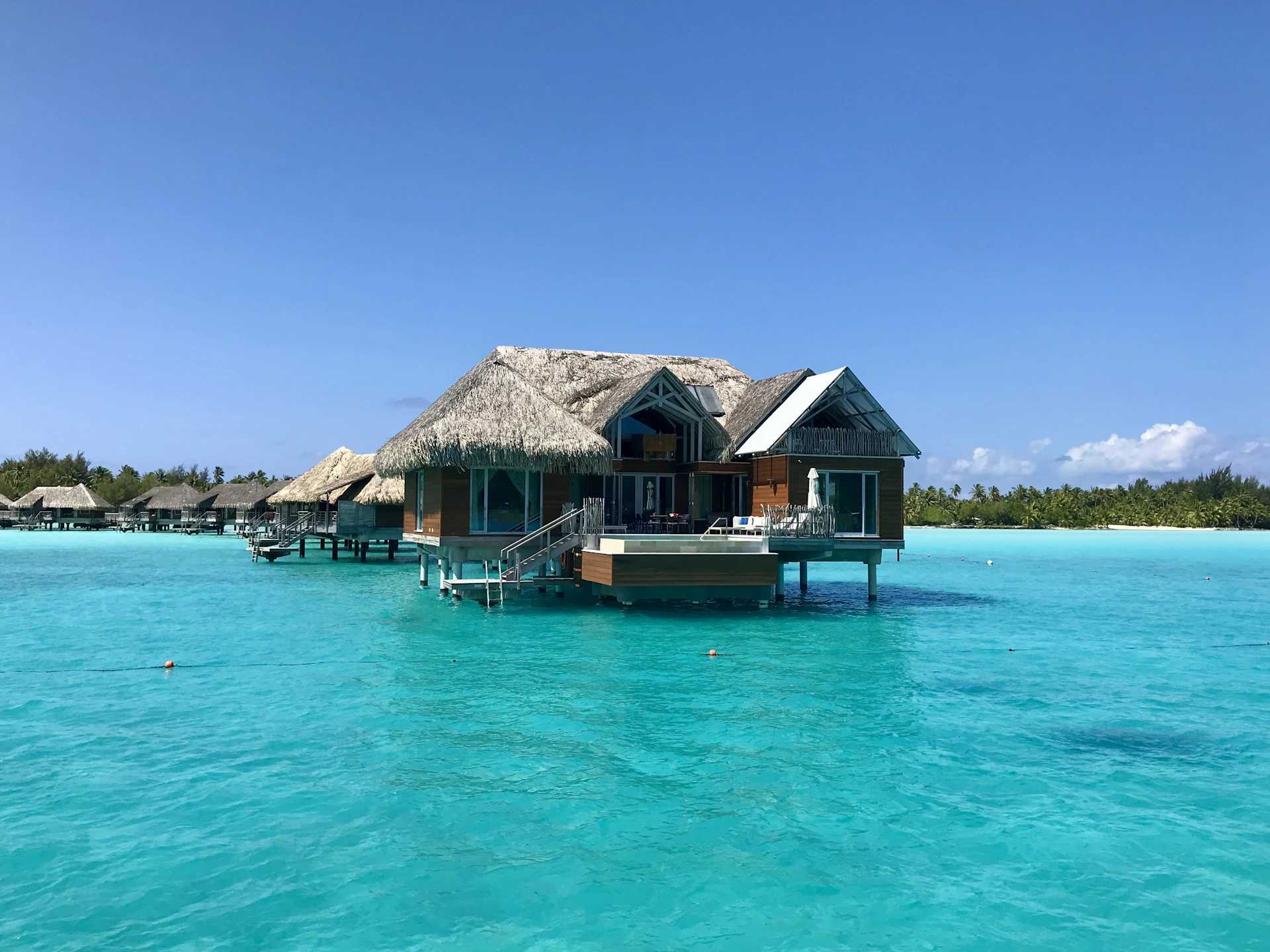 An elegant overwater bungalow in Bora Bora surrounded by crystal-clear turquoise waters under a bright blue sky.