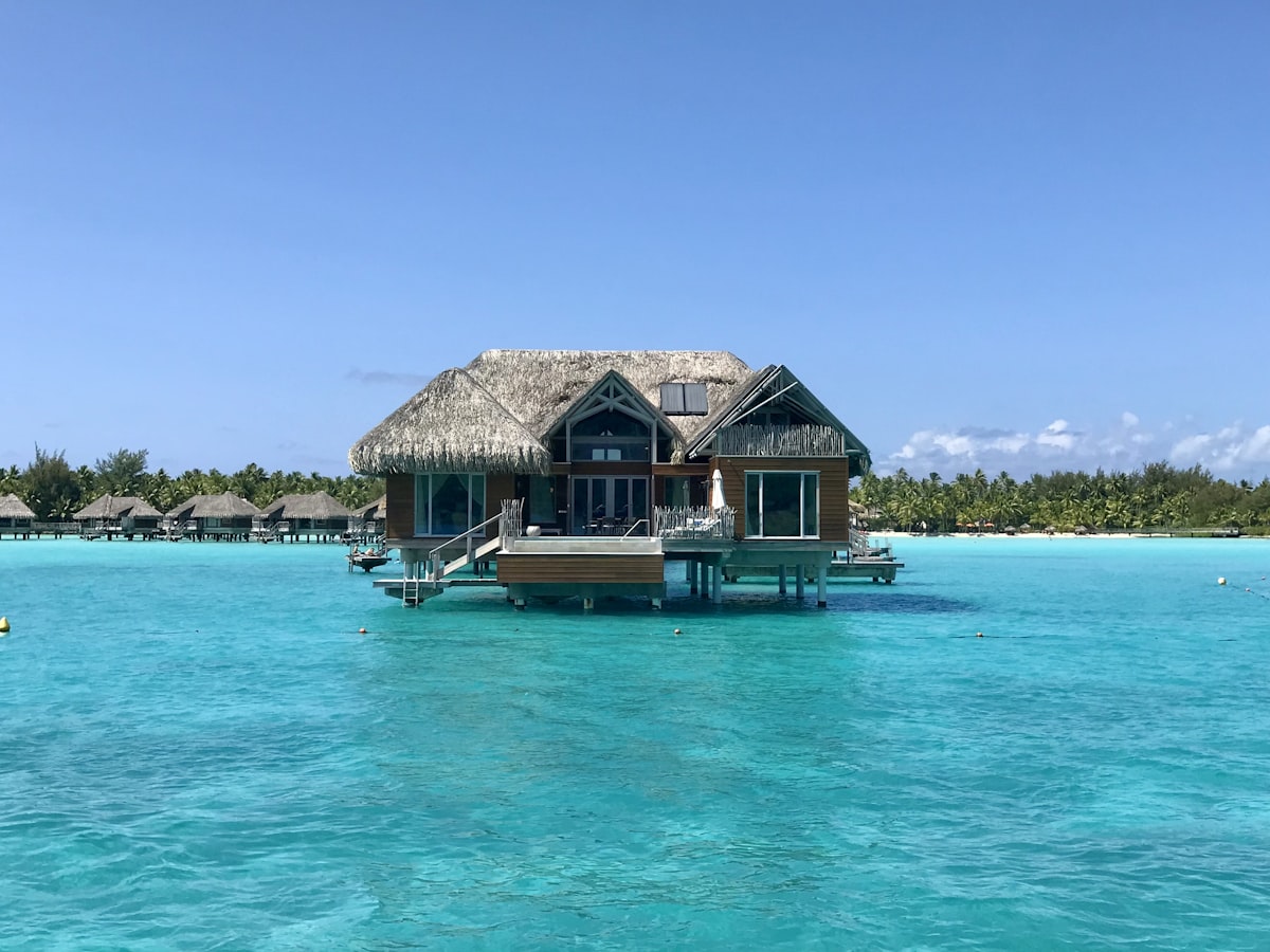 Bora Bora March — a traditional outrigger canoe on the turquoise lagoon with the volcanic peak rising above tropical clouds