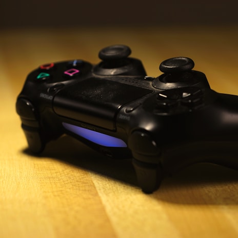 A gaming controller with a dark design resting on a wooden surface, featuring illuminated blue lights.