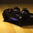 A gaming controller with a dark design resting on a wooden surface, featuring illuminated blue lights.