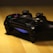 A gaming controller with a dark design resting on a wooden surface, featuring illuminated blue lights.