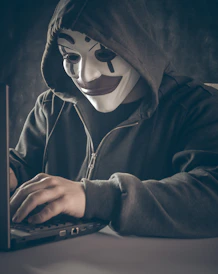 Shadowy figure lurking behind a computer screen, symbolizing online fraud.