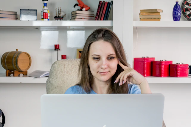 Smiling young woman studying at home with a laptop and books around.