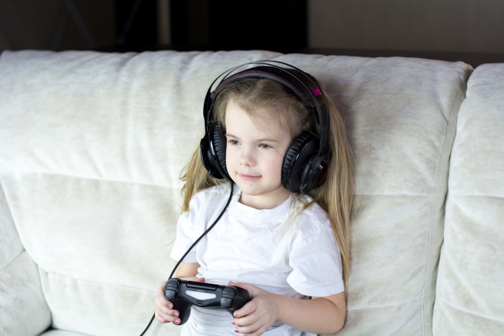 a little girl sitting on a couch with headphones on