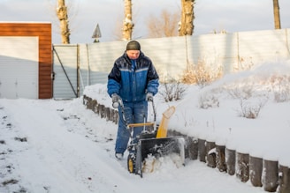 A worker clearing snow from a driveway with a snow blower on a crisp winter morning.