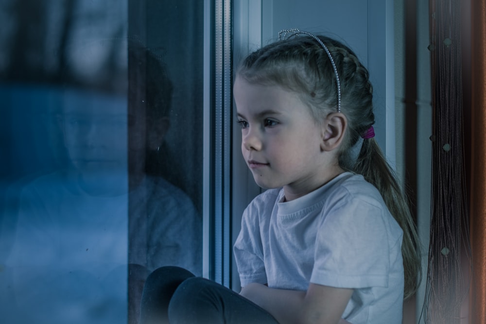 a little girl sitting on a window sill looking out the window