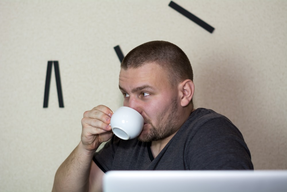 a man drinking a cup of coffee in front of a laptop