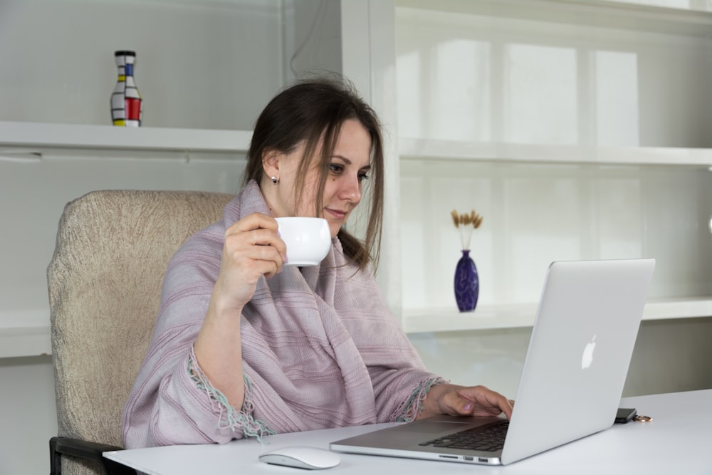 a woman sitting at a desk with a laptop and a cup of coffee
