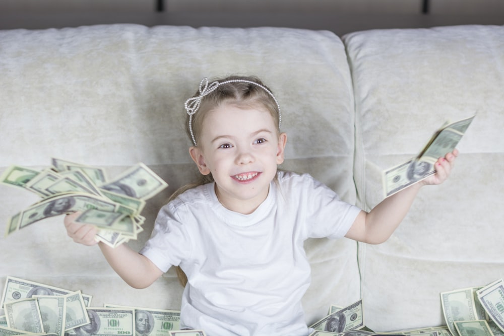 a little girl sitting on a couch holding money