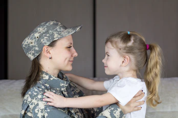 A Service Member in a military uniform hugging a little girl