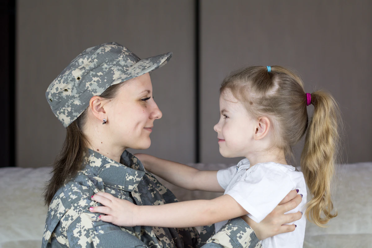 Service member in uniform embracing a young child during a family relocation