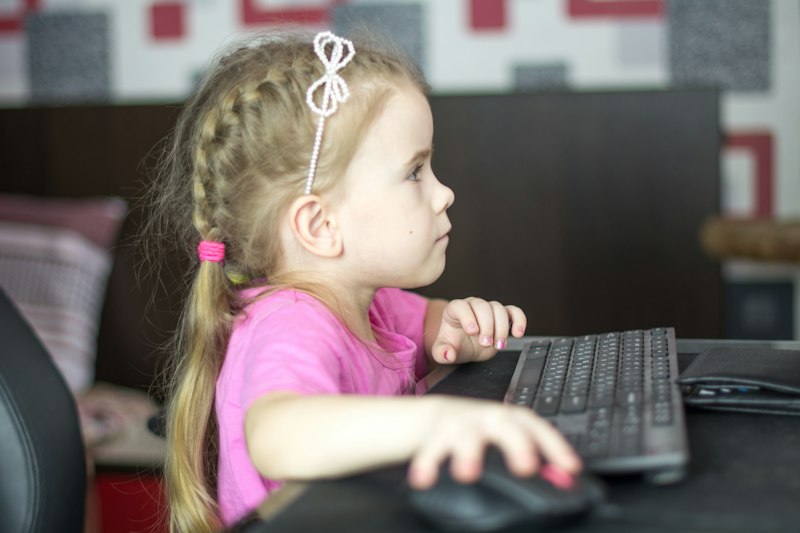 A little girl sitting at a computer keyboard, looking at the screen