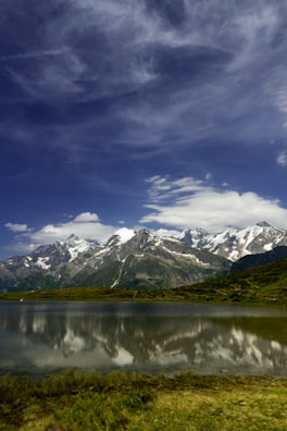 Snow-capped mountains reflecting in a calm alpine lake under a bright blue sky.