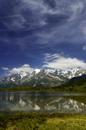 Snow-capped peaks of the Swiss Alps reflected in a crystal-clear mountain lake under a bright blue sky.