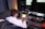 A person seated at a desk is working on a laptop with various audio equipment surrounding them. The setup includes large studio speakers, an external audio interface, and a keyboard. The laptop screen displays a software application with multiple windows open. The room has a professional and tech-focused atmosphere.