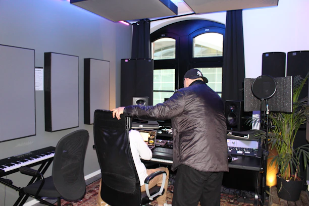 An artist working with a producer in a modern studio filled with instruments and mixing equipment.