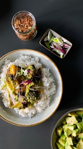 A bowl of uncooked diabetic rice surrounded by fresh vegetables and herbs.