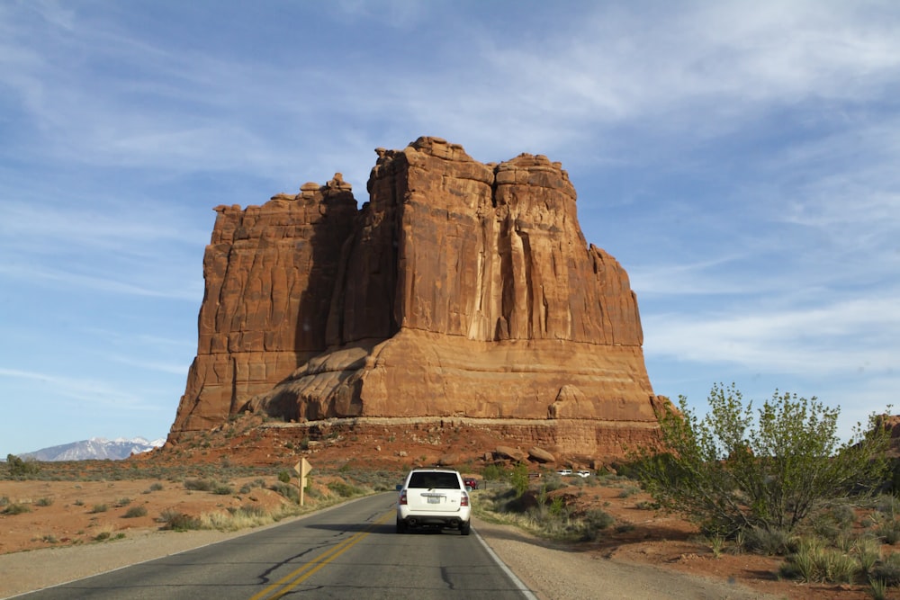 a white van driving down a road next to a tall rock formation