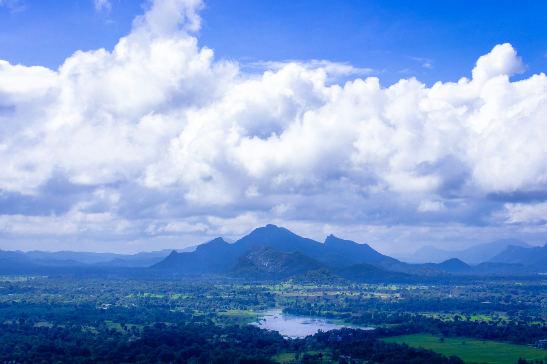 A panoramic view of rolling hills under a vast, clear blue sky dotted with fluffy white clouds.
