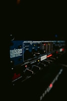 A close-up of professional audio equipment featuring various dials, switches, and displays with labels such as 'lexicon' and 'dbx'. The focus is primarily on the control panel with illuminated LEDs and digital indicators.