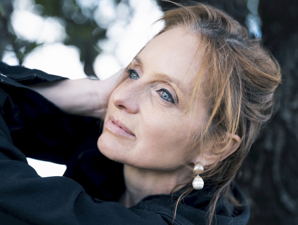 a woman leaning against a tree with her hand on her shoulder