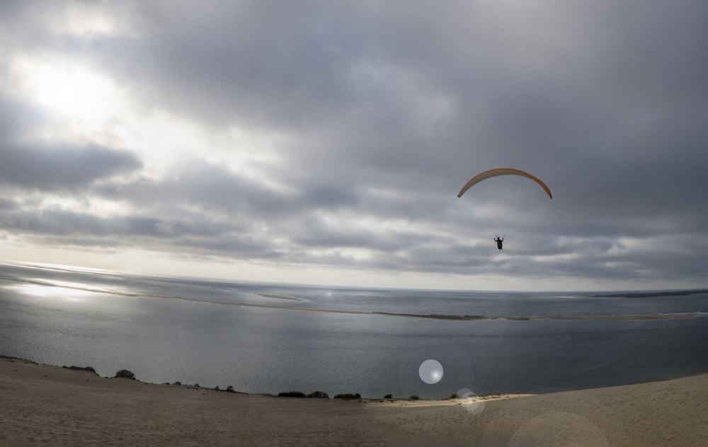 a paraglider flying over the ocean under a cloudy sky