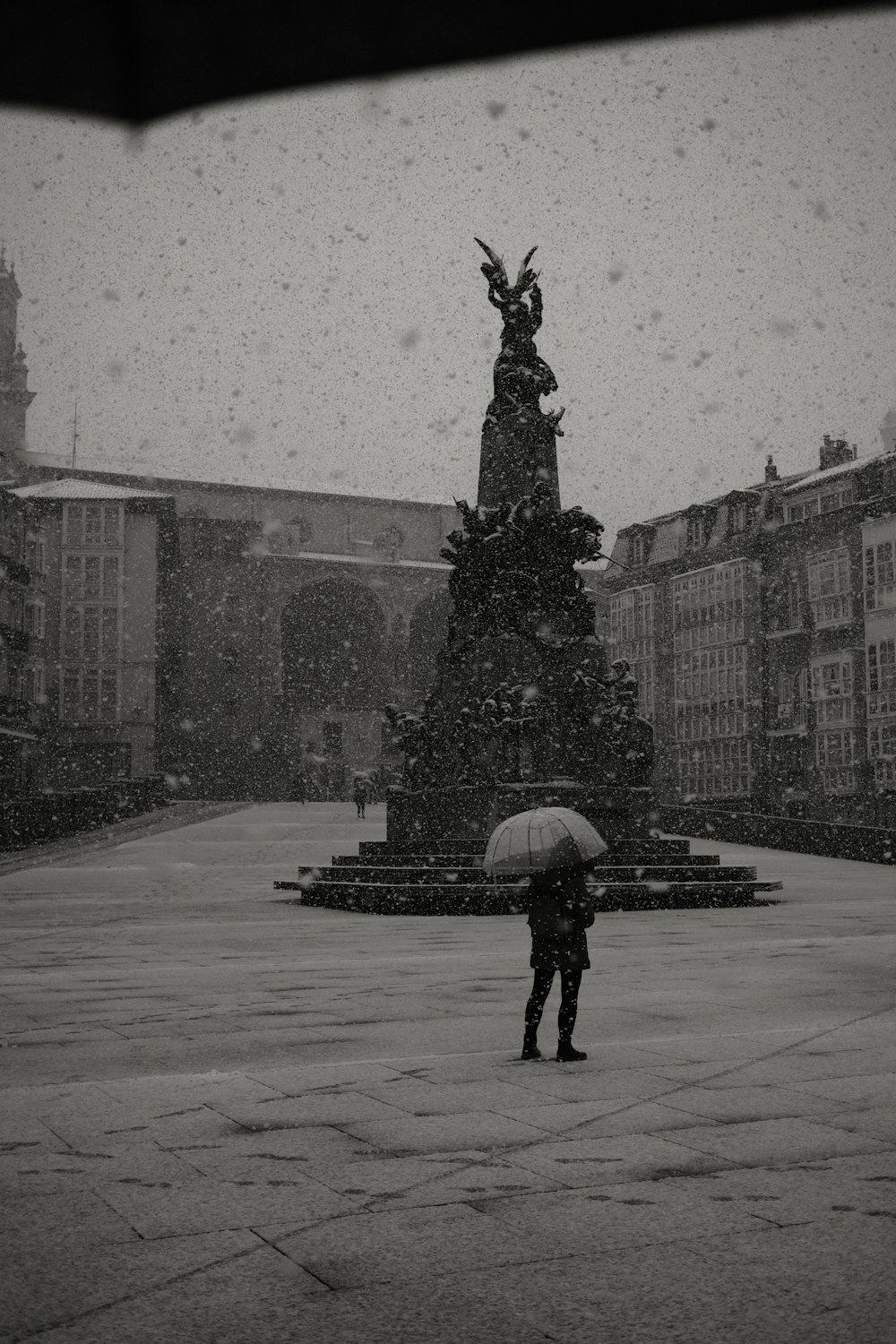 a person holding an umbrella standing in front of a statue
