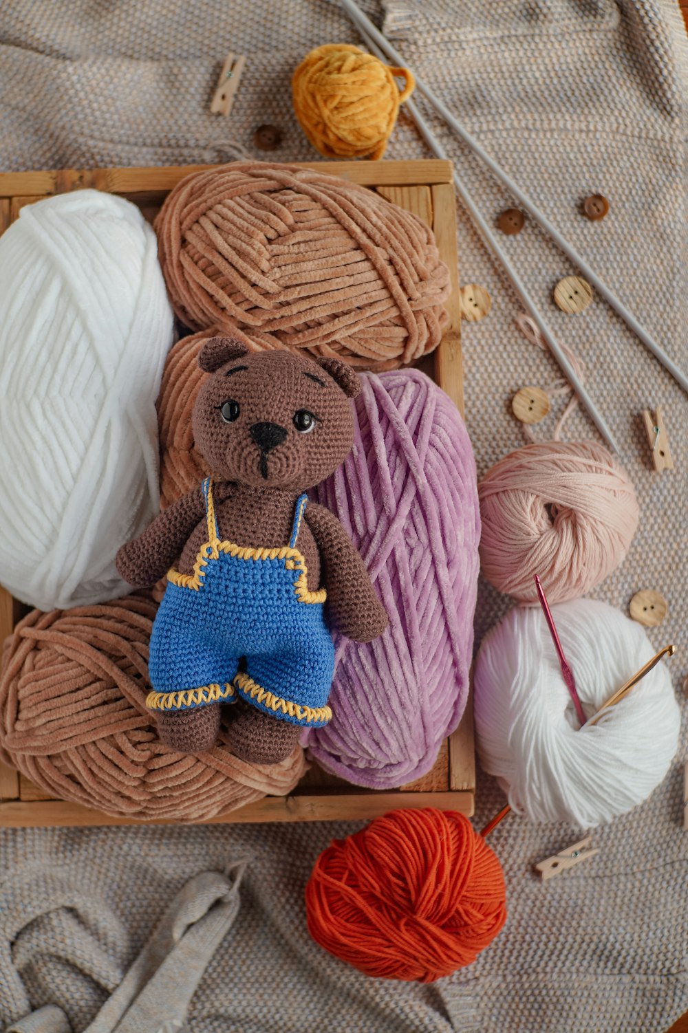 a teddy bear sitting on top of a wooden box next to balls of yarn