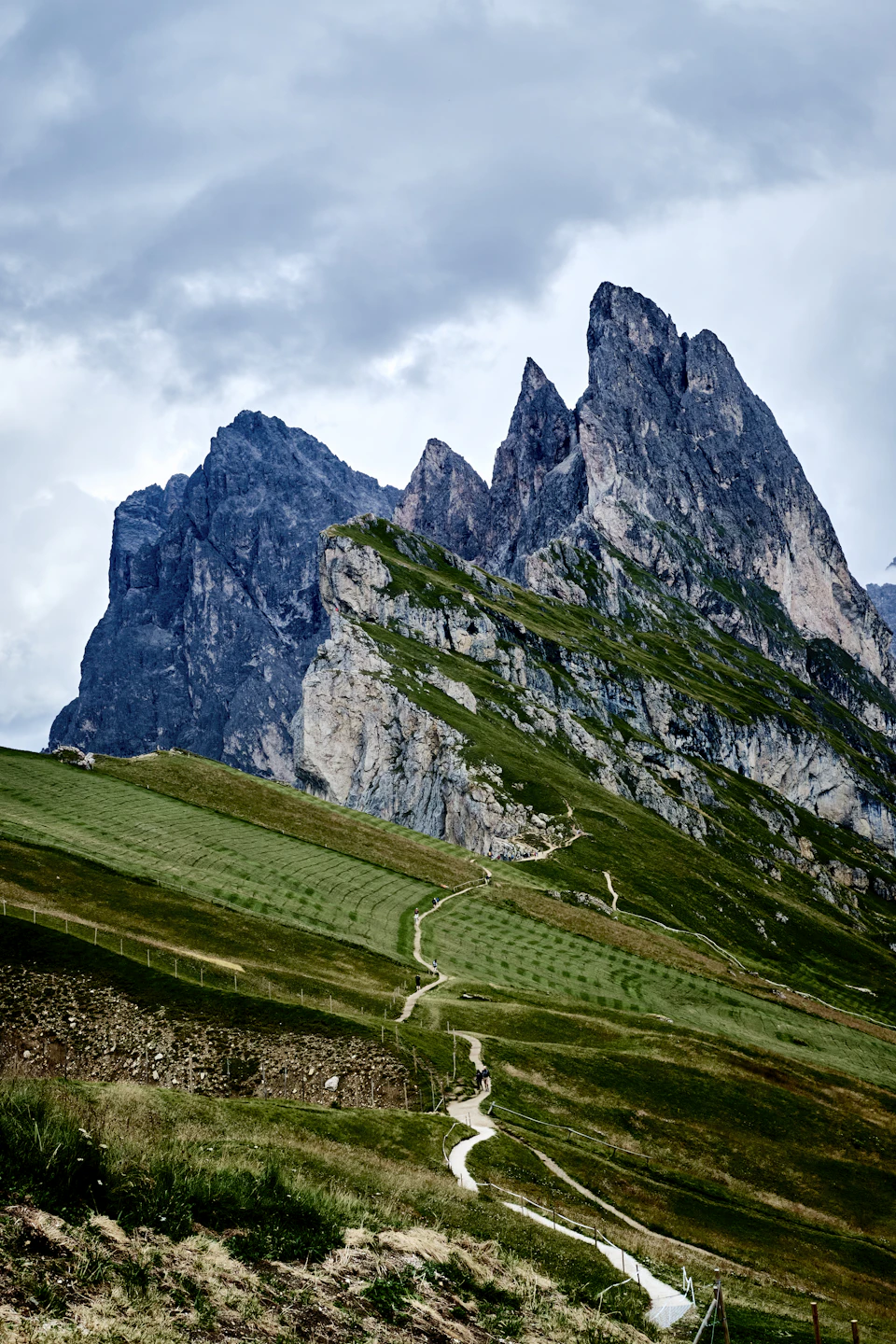 Mountainous landscape features a winding path through lush green fields and towering mountains