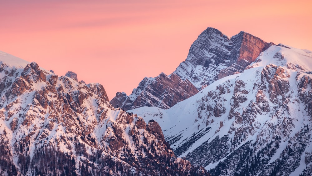 a mountain range covered in snow at sunset