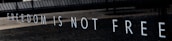 The wall displays the phrase 'FREEDOM IS NOT FREE' in large, bold white letters against a dark background, suggesting a somber and reflective atmosphere.