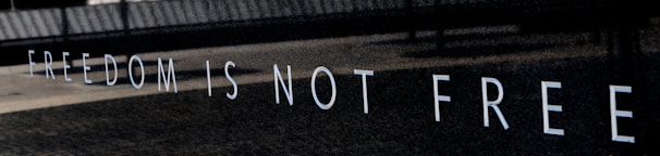 The wall displays the phrase 'FREEDOM IS NOT FREE' in large, bold white letters against a dark background, suggesting a somber and reflective atmosphere.
