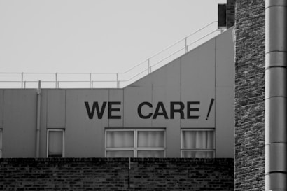A portion of a building with the phrase 'WE CARE!' written in large, bold letters on its upper section. The building features a flat roof with railing and several windows just below the text.