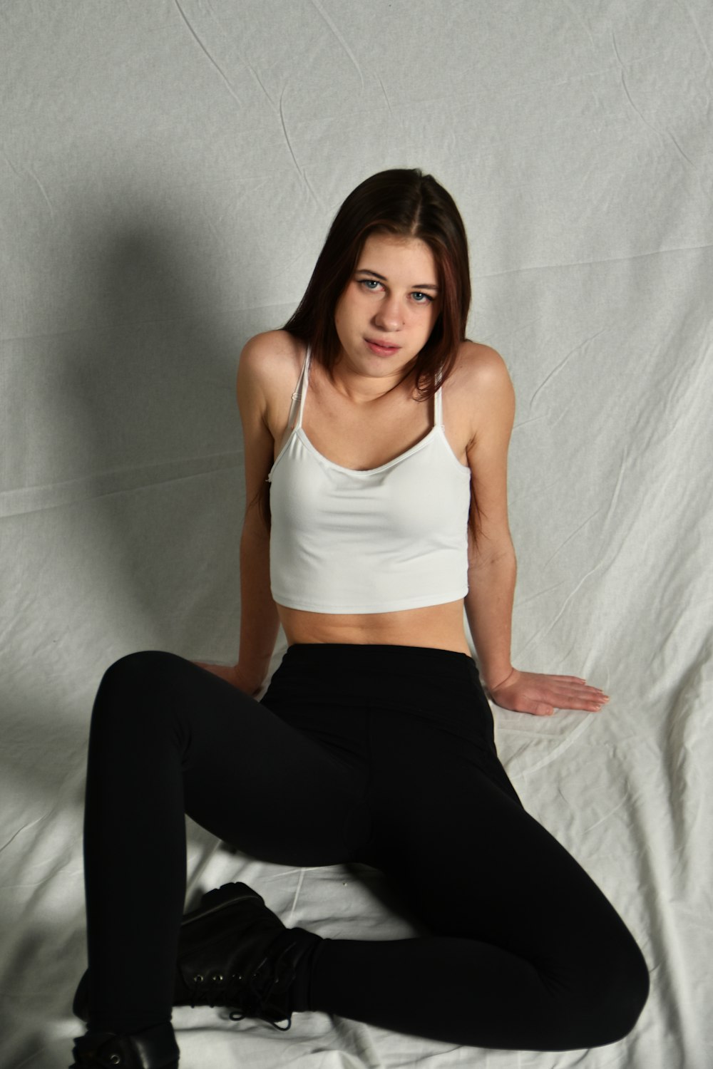 a woman sitting on a bed in a white top and black pants