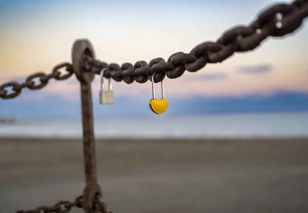a yellow heart hanging from a chain on a beach