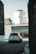 A white SUV is driving down a quiet urban street with a large building in the background featuring signage for 'Storage' and 'Green Box'. The scene has a modern, industrial feel with sleek architecture and muted tones.