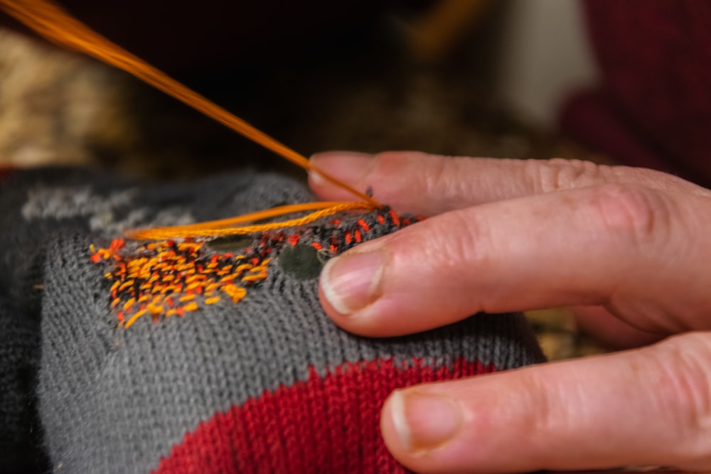 a person is knitting a sweater with an orange needle