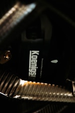 A close-up view of a carbon fiber texture, highlighting a component labeled with the word 'Koenigsegg'. The carbon fiber patterns appear shiny and reflect light, giving a glossy effect to the surface.