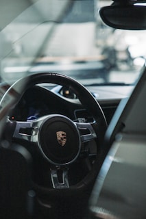 A close-up view of a car's interior featuring a steering wheel with a prominent logo. The sleek design and materials of the car's dashboard are partially visible, hinting at luxury and sophistication.