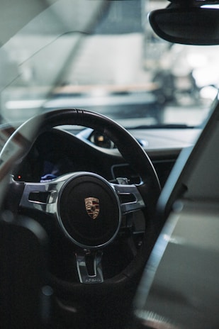 A close-up view of a car's interior featuring a steering wheel with a prominent logo. The sleek design and materials of the car's dashboard are partially visible, hinting at luxury and sophistication.