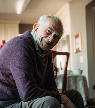 A warm, smiling support worker gently assisting an elderly woman with her daily routine in a bright, cozy living room.