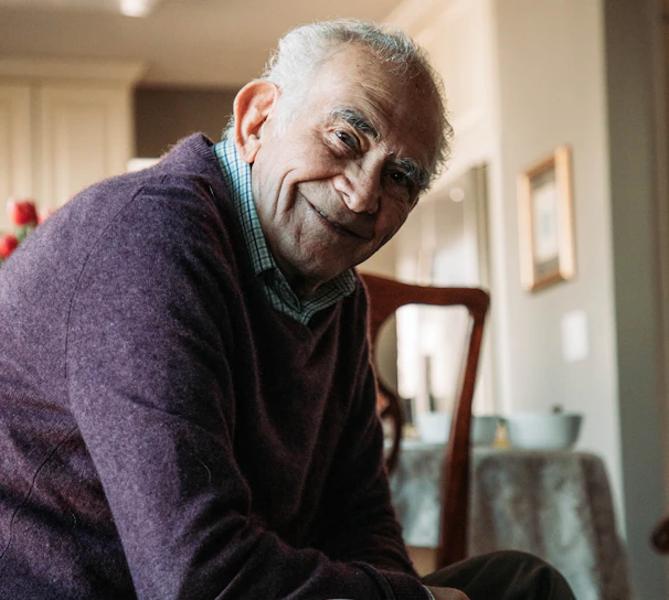 A warm, smiling support worker gently assisting an elderly woman with her daily routine in a bright, cozy living room.