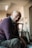 A caregiver gently assisting an elderly woman with a warm smile in a bright, inviting living room.