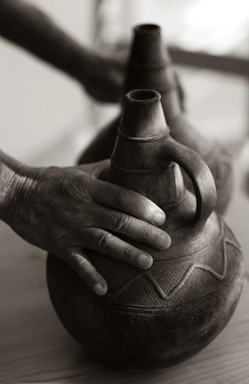 Hands holding a freshly crafted clay pot with natural color patterns.