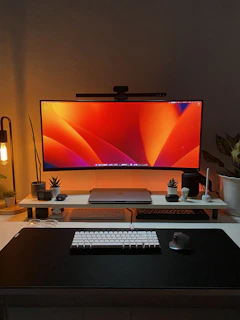 A modern desktop setup with a large monitor, keyboard, and mouse, styled with red and black accents.