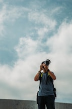 A friendly photographer holding a camera, standing in front of a modern home with a blue sky background.