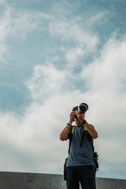 A friendly photographer holding a camera, standing in front of a modern home with a blue sky background.